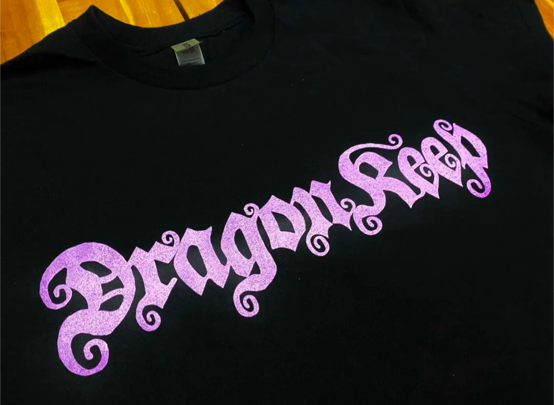 Close up - Black tee shirt with purple logo printed in front which says Dragon Keep